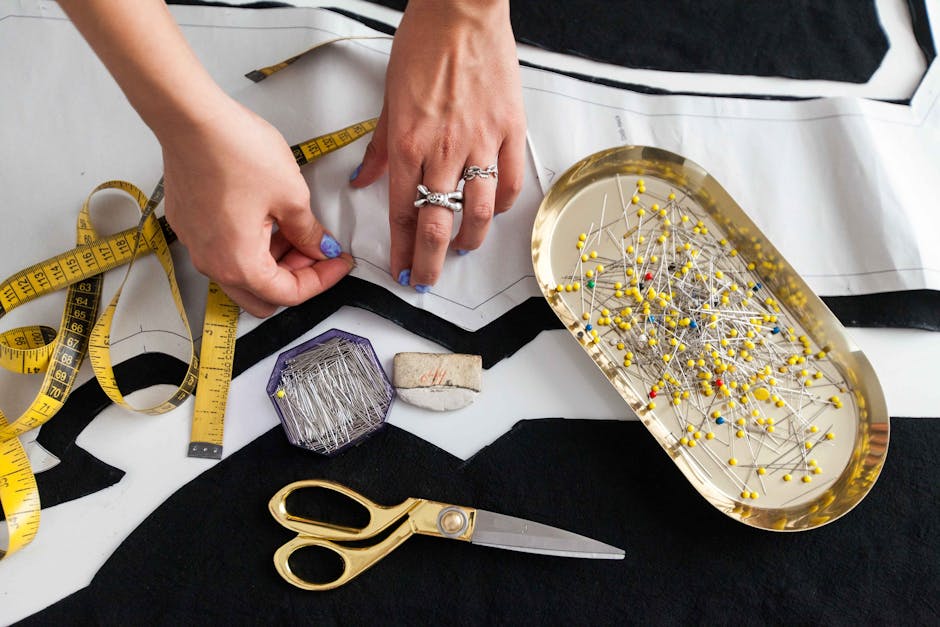 A pair of hands working on garment design with sewing tools on a table.