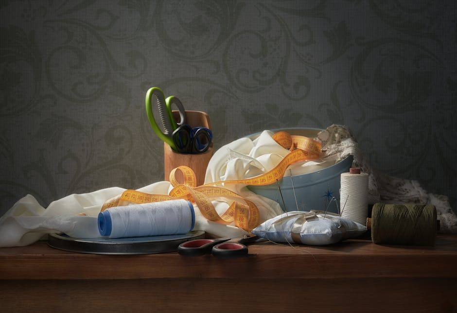 A classic still life of sewing materials including fabric, threads, scissors, and tape measure.