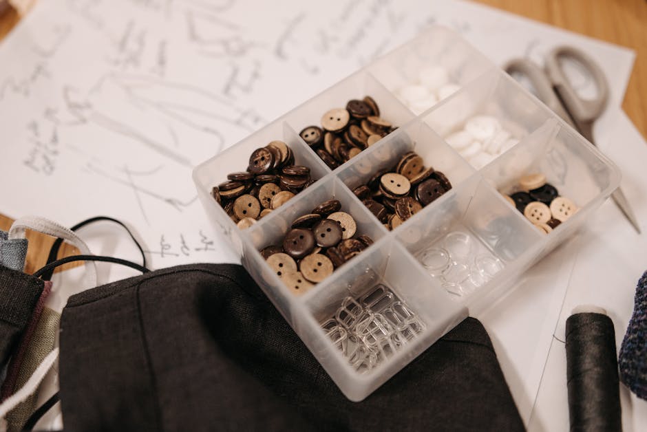 A collection of buttons, sketches, and sewing tools on a designer's desk, showcasing creative fashion work.